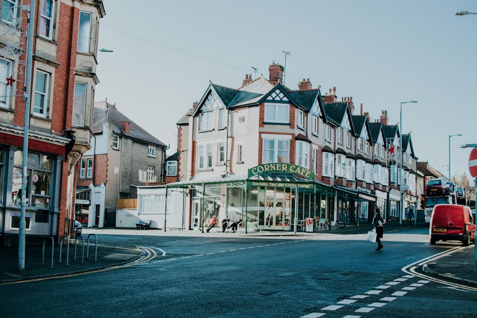 Outdoor seating area of a cafe on Station Road Elmstead featuring several red cushioned chairs with black wooden frames arranged around dark wooden tables. The flooring consists of patterned tiles wit